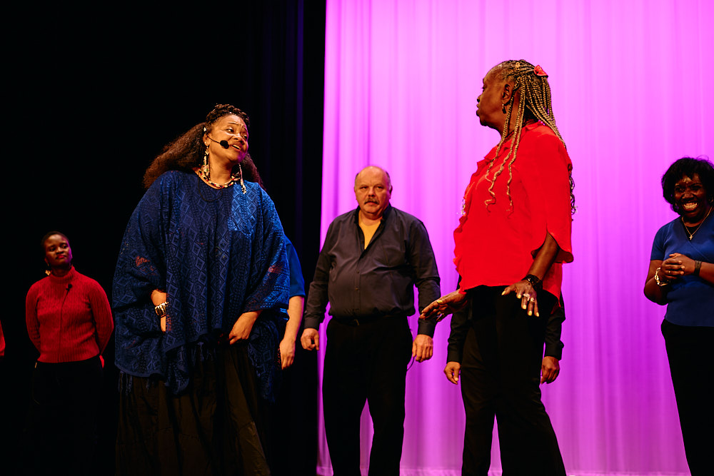 A soloist sings under a spotlight, with choir members visible behind her.