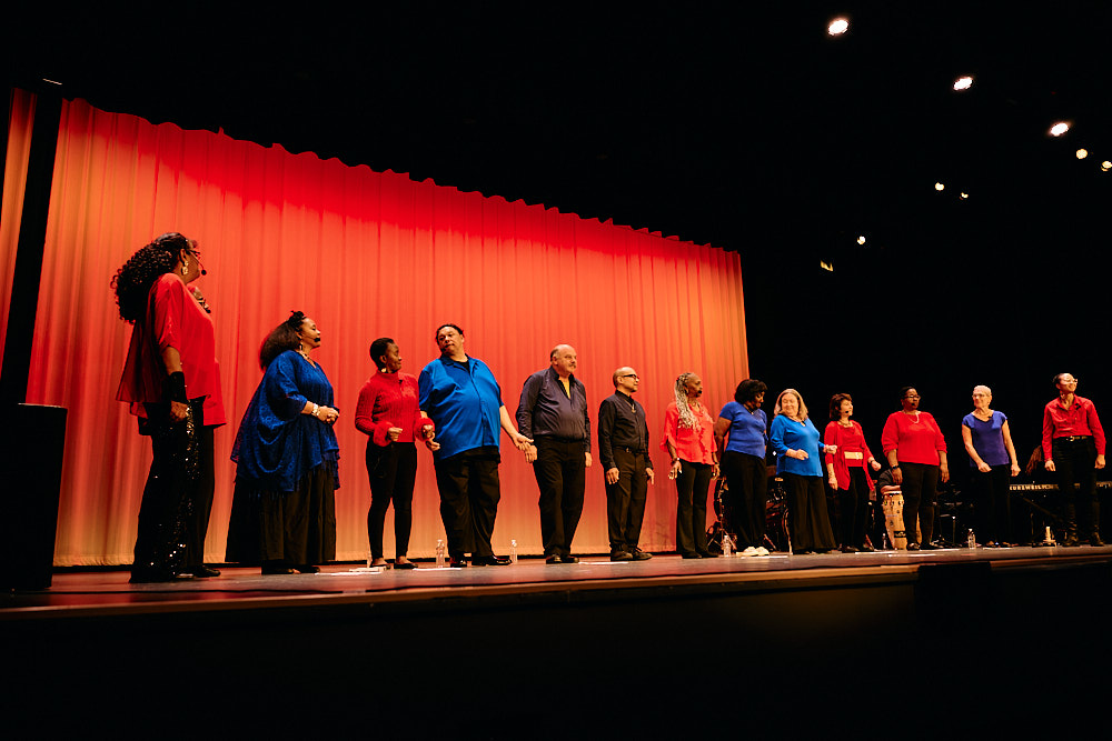 A soloist sings with a raised fist, fellow performers singing behind her.